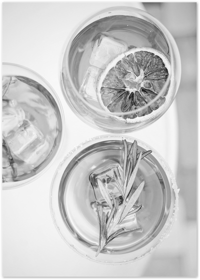 Black and white overhead photo of three cocktail glasses with ice, citrus and rosemary