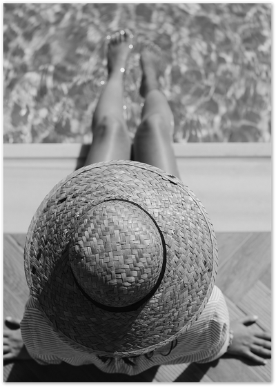 Black and white photo of a woman lying poolside with a straw hat on her chest