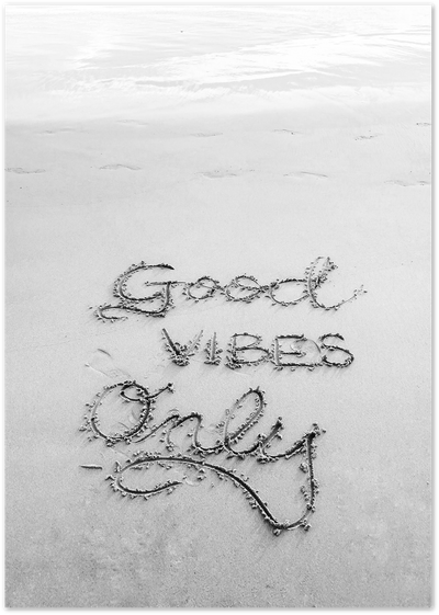 Black-and-white photo of 'Good Vibes Only' handwritten in beach sand near the shoreline