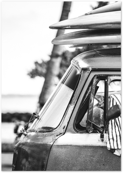 Black and white close-up photo of a vintage van with surfboards on the roof rack near a palm tree