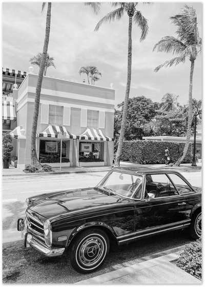 Black and white photo of a vintage Mercedes convertible parked under palm trees near a striped building