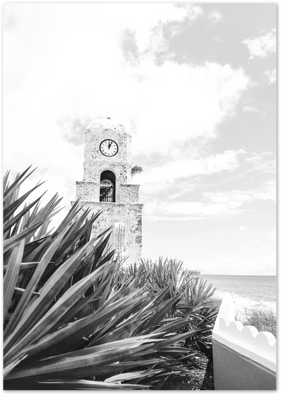 Black and white photo of a stone clock tower with palm leaves and ocean in background